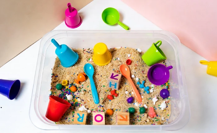 Bacia sensorial com arroz colorido, colheres e objetos para exploração de crianças pequenas